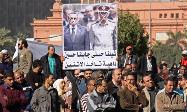 [A man carrying a banner which compares head of military council Hussein Tantawi to toppled president Hosni Mubarak on Friday of Regaining Honor, 23 December 2011. Image by Mai Shaheen]