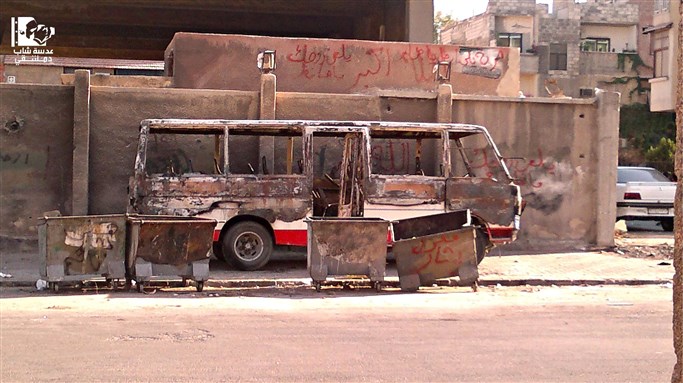 [Destroyed bus and graffiti in Zahira, Damascus. 13 September 2012. Image via Lens Young Dimashqi.]